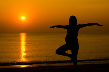 Silhouette of pregnant doing yoga on the beach in morning