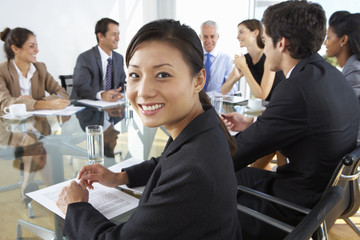 Asian Businesswoman Sitting Around Boardroom Table With Colleagues