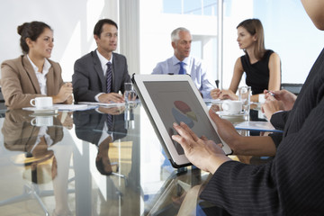 Close Up Of Businesswoman Using Tablet Computer During Board Meeting Around Glass Table