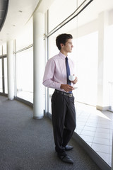 Young Businessman Standing In Corridor Of Modern Office Building Drinking Coffee