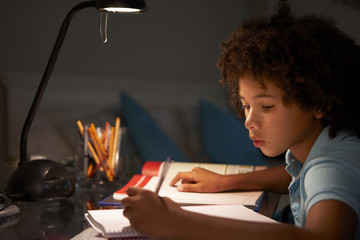 Young Boy Studying At Desk In Bedroom In Evening
