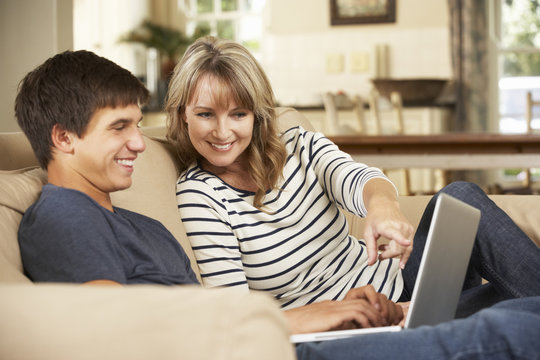 Mother With Teenage Son Sitting On Sofa At Home Using Laptop