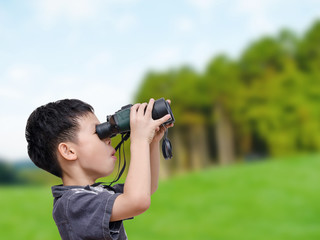 Young Asian boy using binoculars in forest