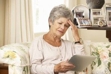 Fototapeta premium Frustrated Retired Senior Woman Sitting On Sofa At Home Using Digital Tablet