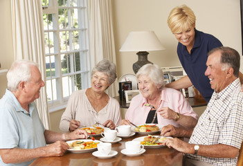 Group Of Senior Couples Enjoying Meal Together In Care Home With Home Help