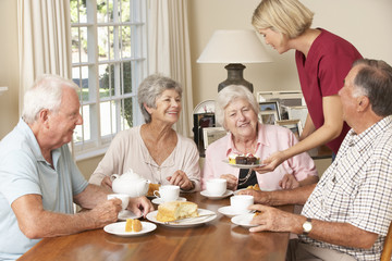 Group Of Senior Couples Enjoying Afternoon Tea Together At Home With Home Help