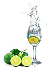 Lime splashing into glass of water on white background