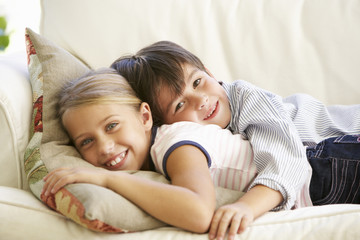 Two Children Relaxing On Sofa At Home