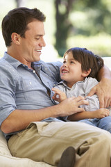 Father And Son Sitting On Sofa At Home