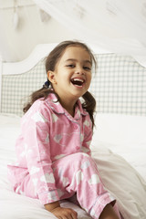 Young Girl Wearing Pajamas Sitting On Bed