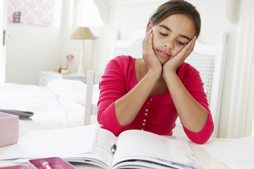 Bored Young Girl Doing Homework At Desk In Bedroom