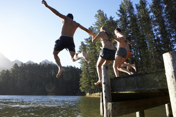 Group Of Young People Jumping From Jetty Into Lake