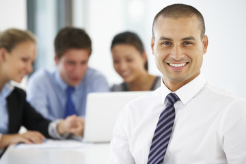 Portrait Of Male Executive With Office Meeting In Background