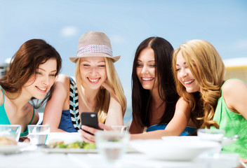 girls looking at smartphone in cafe on the beach