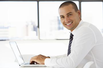 Businessman Sitting At Desk In Office Using Laptop