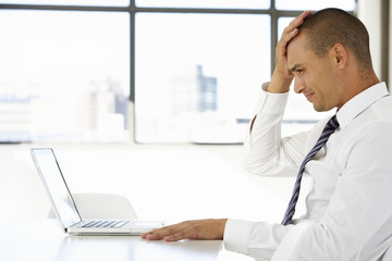 Fototapeta na wymiar Frustrated Businessman Sitting At Desk In Office Using Laptop