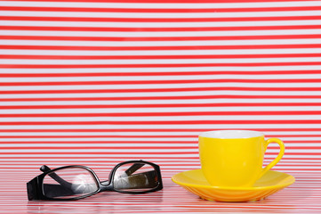 Yellow coffee cup with glasses on red texture line.