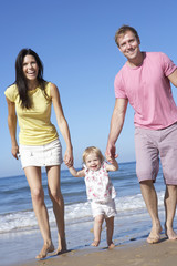 Family With Young Daughter Walking Along Beach Together