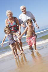 Grandparents And Grandchildren Running Along Beach