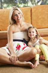 Mother And Daughter Sitting In Front Of Sofa