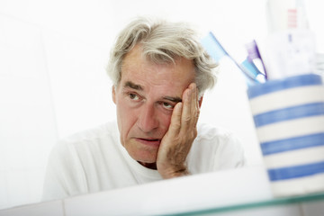 Tired Senior Man Looking At Reflection In Bathroom Mirror