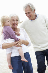 Grandparents And Granddaughter Walking Along Beach Together