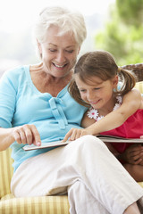Grandmother And Granddaughter Reading Book On Garden Seat