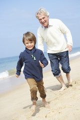 Grandfather And Grandson Running Along Beach