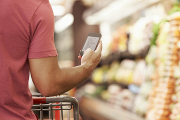 Close Up Of Man Reading Shopping List From Mobile Phone In Supermarket