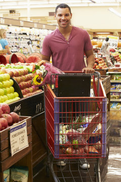 Man Pushing Trolley By Fruit Counter In Supermarket