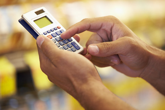 Man In Grocery Aisle Of Supermarket Using Calculator