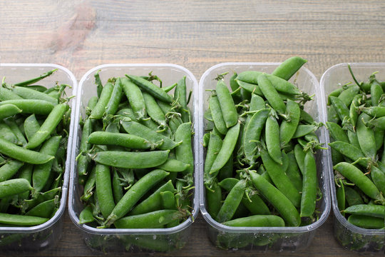 fresh green peas in a plastic container on a wooden background