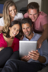 Fototapeta na wymiar Group Of Friends Sitting On Sofa Looking At Digital Tablet