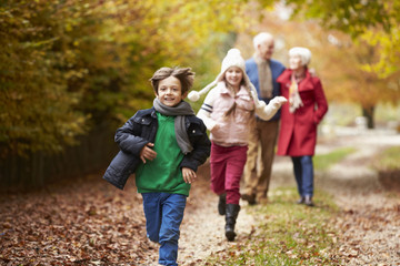 Grandparents With Grandchildren Running Along Autumn Path