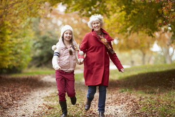 Grandmother Running Along Autumn Path With Granddaughter