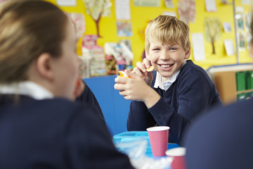 Schoolchildren Sitting At Table Eating Packed Lunch