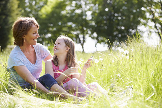 Grandmother And Granddaughter Sitting In Summer Field