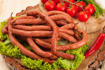 Smoked meat sausage salami with bright summer vegetables and bread on wooden background