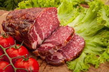 Smoked meat sausage salami with bright summer vegetables and bread on wooden background