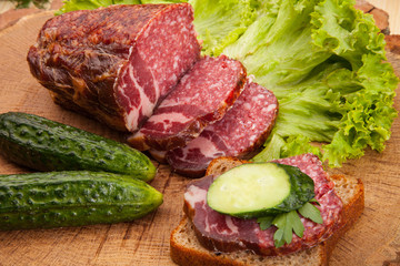 Smoked meat sausage salami with bright summer vegetables and bread on wooden background