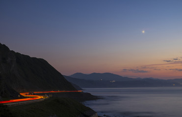 Car lights in the road at night, by the sea