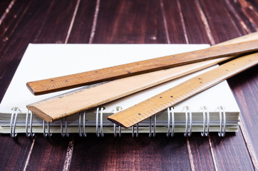 Wooden ruler and notebook on wooden board background