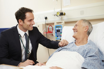 Doctor Sitting By Male Patient's Bed In Hospital