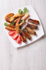 Pork ribs, potatoes and tomatoes on a plate top view vertical 
