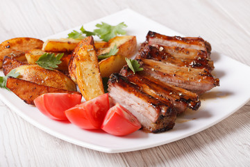 Pork ribs, potatoes and tomatoes on a plate close-up
