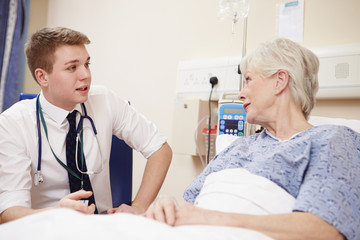 Obraz premium Doctor Sitting By Senior Female Patient's Bed In Hospital