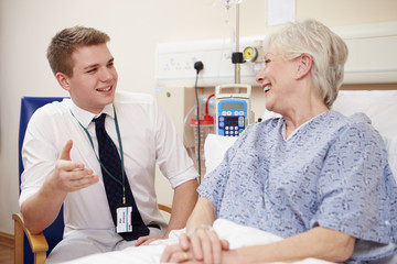 Doctor Sitting By Senior Female Patient's Bed In Hospital