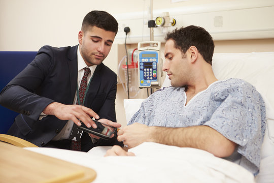 Doctor Sitting By Male Patient's Bed Using Digital Tablet