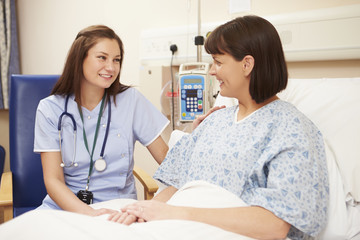 Nurse Sitting By Female Patient's Bed In Hospital