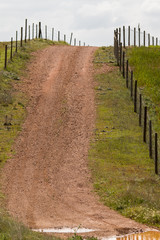 Obraz premium View of a hill with a fence and dirt road in Alentejo, Portugal.